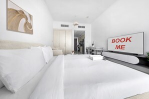 A modern hotel room with a large bed, a TV, and a 'BOOK ME' sign. - Stayshort - Damac Hills Sleeps 2 Near Golf Courses (Dubai)