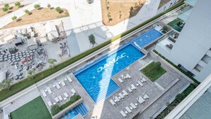 An aerial view of a modern hotel with a large swimming pool, outdoor seating areas, and a landscaped courtyard. - Stayshort - Business Bay for 4 People With a Fabulous Pool (Dubai)
