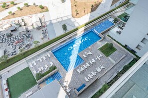 An aerial view of a modern hotel with a large swimming pool, outdoor seating areas, and a landscaped courtyard. - Stayshort - Business Bay for 4 People With a Fabulous Pool (Dubai)