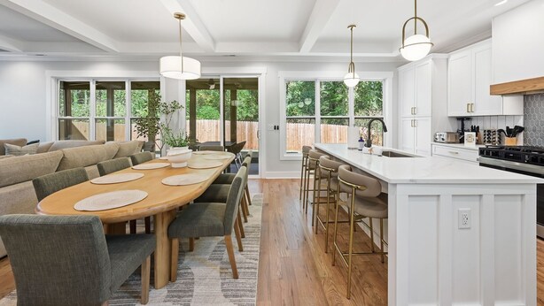 A modern kitchen with white cabinetry, a large island with bar stools, and pendant lighting. - New! Modern Luxurious Woodland Retreat 5 Bedroom Home (Scottdale)
