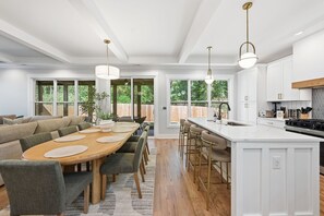 Uma cozinha moderna com armários brancos, uma ilha grande com banquetas e iluminação pendente.