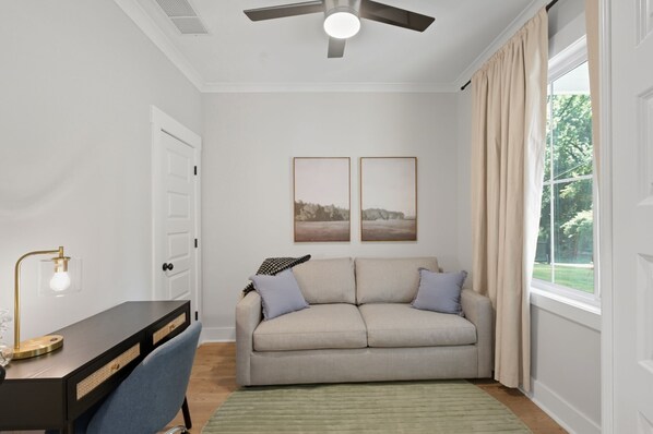 Une pièce comprenant un bureau, un canapé, un ventilateur de plafond et deux tableaux encadrés accrochés au mur.