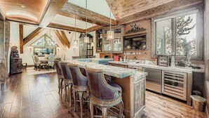 A spacious kitchen with a large island, bar stools, and a dining area with a high ceiling and wooden beams. - Fairway Drive Retreat 6 Bedroom Home (Avon)