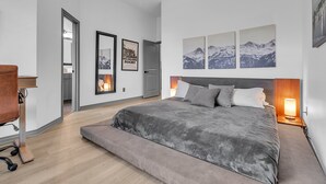 A modern bedroom with a large bed, a desk, and a chair. There are framed pictures on the wall and a door leading to another room. - Relaxing College Station Retreat With Hot Tub 3 Bedroom Home (College Station)