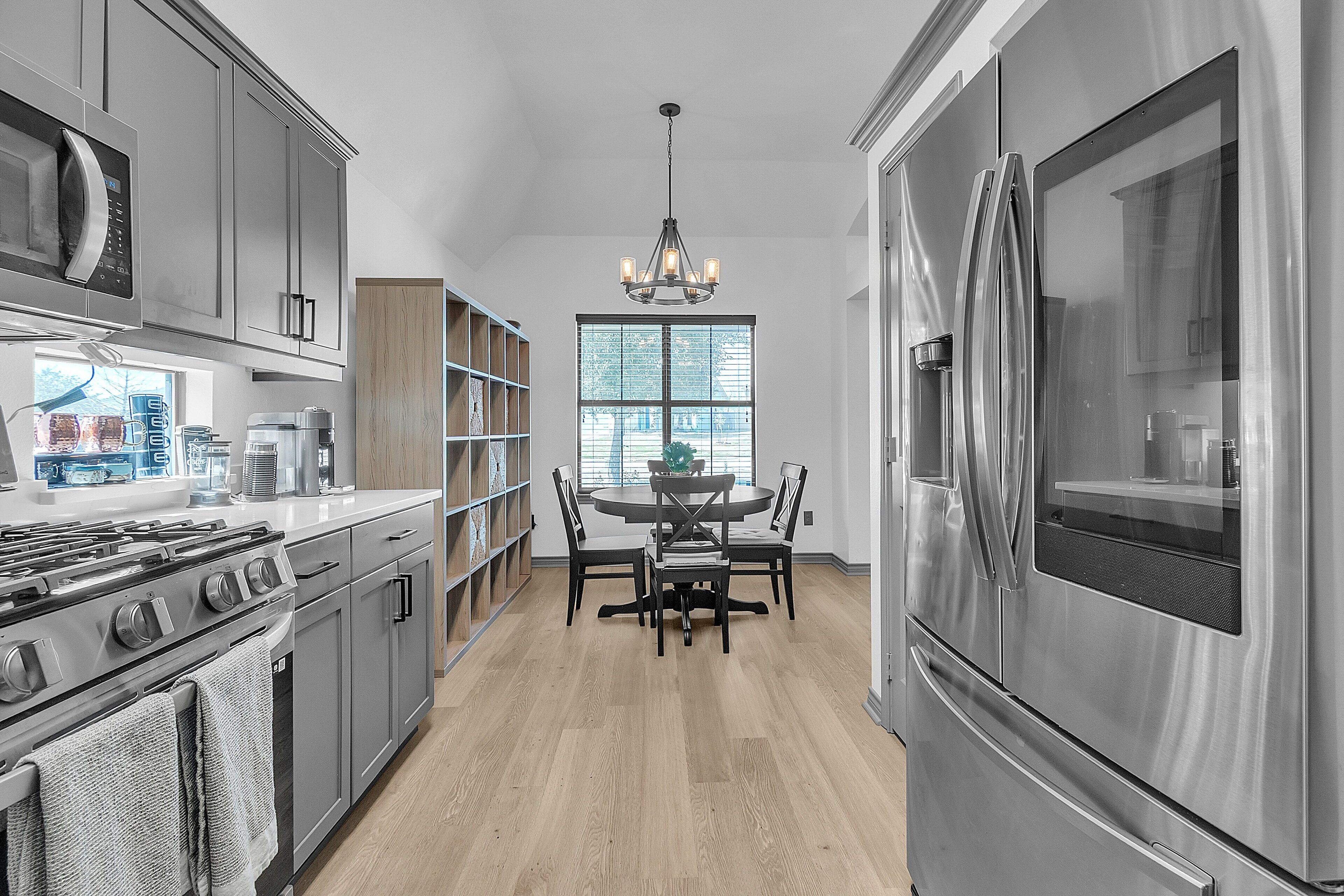 A modern kitchen with stainless steel appliances, a dining area with a chandelier, and wooden shelves.