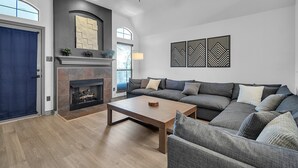 A modern living room with a fireplace, a large gray sectional sofa, a coffee table, and a ceiling fan. - Relaxing College Station Retreat With Hot Tub 3 Bedroom Home (College Station)
