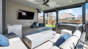 A modern outdoor living area with a flat-screen TV, seating, and a hot tub. - Relaxing College Station Retreat With Hot Tub 3 Bedroom Home (College Station)