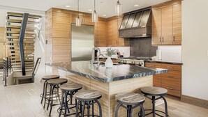 A modern kitchen with wooden cabinets, a large island with stools, stainless steel appliances, and pendant lighting.