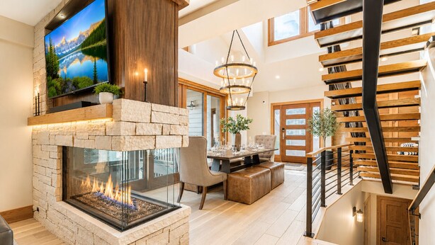 A modern living room with a stone fireplace, a flat-screen TV, and a staircase with wooden railings.