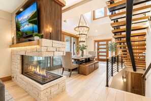 Un salon moderne doté d’une cheminée en pierre, d’un téléviseur à écran plat et d’un escalier avec des rampes en bois.