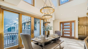 A spacious dining area with a large table set for four, a chandelier, and a view of the outside through large windows.