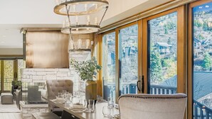 A dining area with a stone fireplace, a chandelier, and a view of a mountainous landscape through large windows.