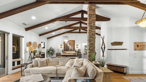 Un salon spacieux avec un grand canapé d’angle, une table basse et un pilier en pierre. Les murs sont ornés d’objets décoratifs et un lustre est suspendu au plafond.