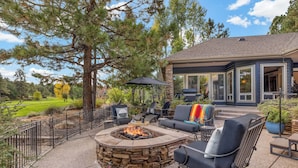 Une terrasse dotée d’un foyer en pierre, de mobilier d’extérieur et offrant une vue sur un terrain de golf.