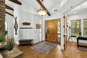 Un'ampia stanza con pavimento in legno, una grande porta in legno, un lampadario e decorazioni murali rustiche.