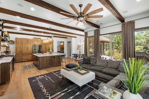 A spacious kitchen with wooden cabinets, a central island, and modern appliances. There is a dining area with a table and chairs, and a living room with a sofa and a coffee table.