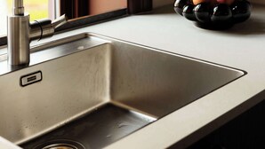 A kitchen sink with a modern faucet, a bowl of fruit on the counter, and a window in the background.