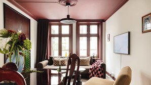 A cozy living room with a dining table, chairs, a sofa, and a large window with curtains.