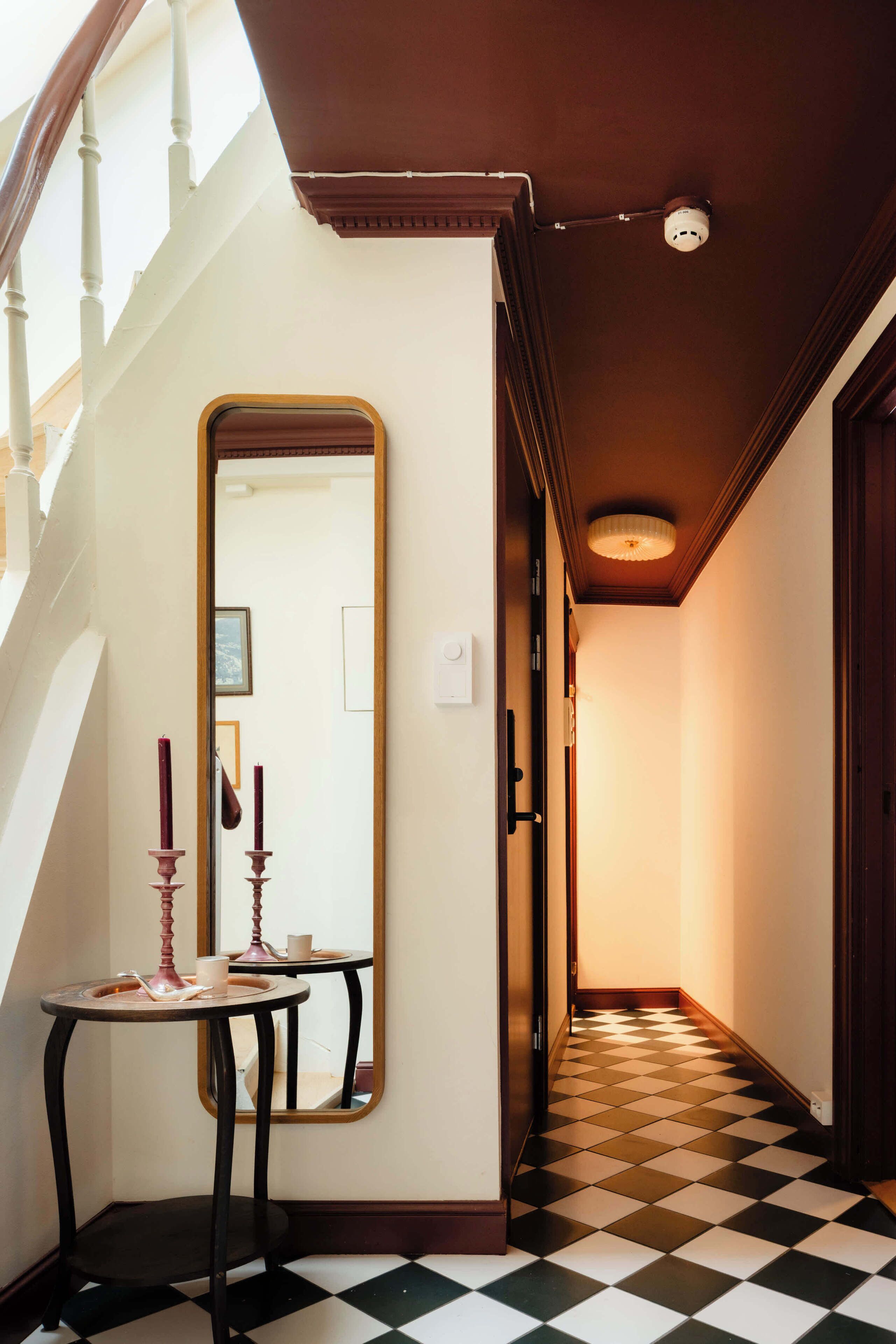 Un couloir avec un sol à carreaux, un miroir et une table ornée de bougies.