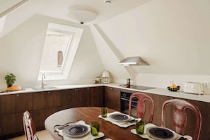 A modern kitchen with dark wooden cabinets, a white countertop, and a dining area with a round table and red chairs.