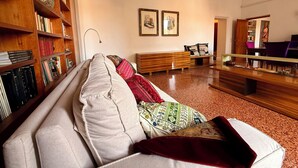 Uma sala de estar com sofá, estante de madeira, um banco de madeira e uma mesa de jantar com cadeiras.