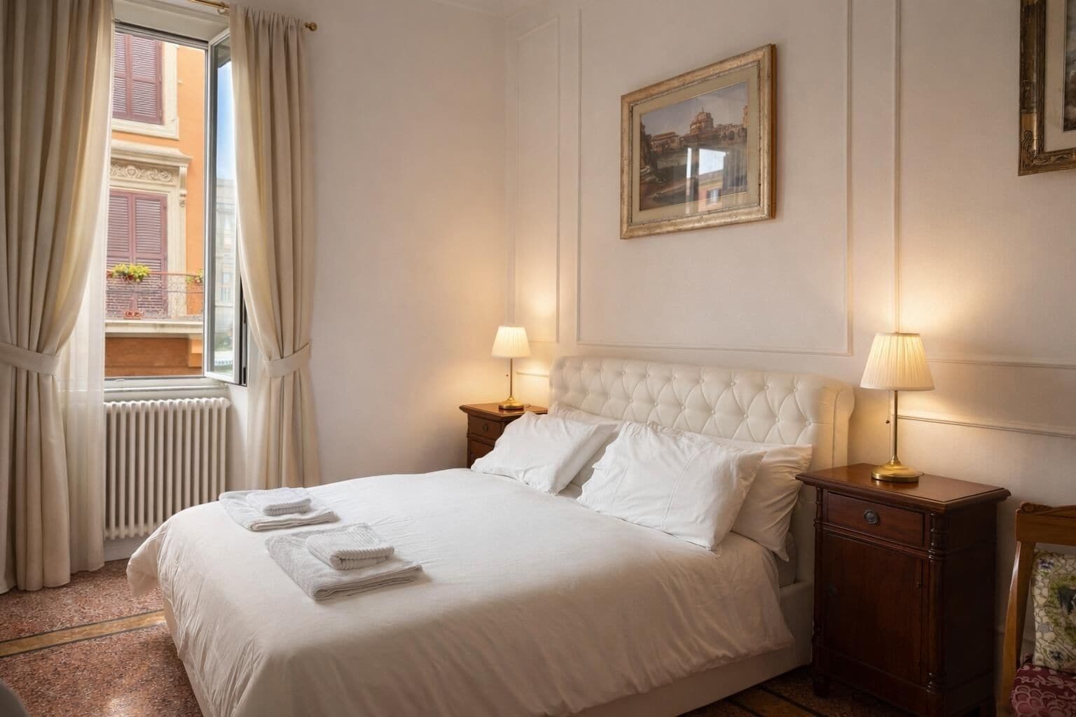 A neatly made bed with white linens and two pillows, a window with curtains, a radiator, and a framed picture on the wall.