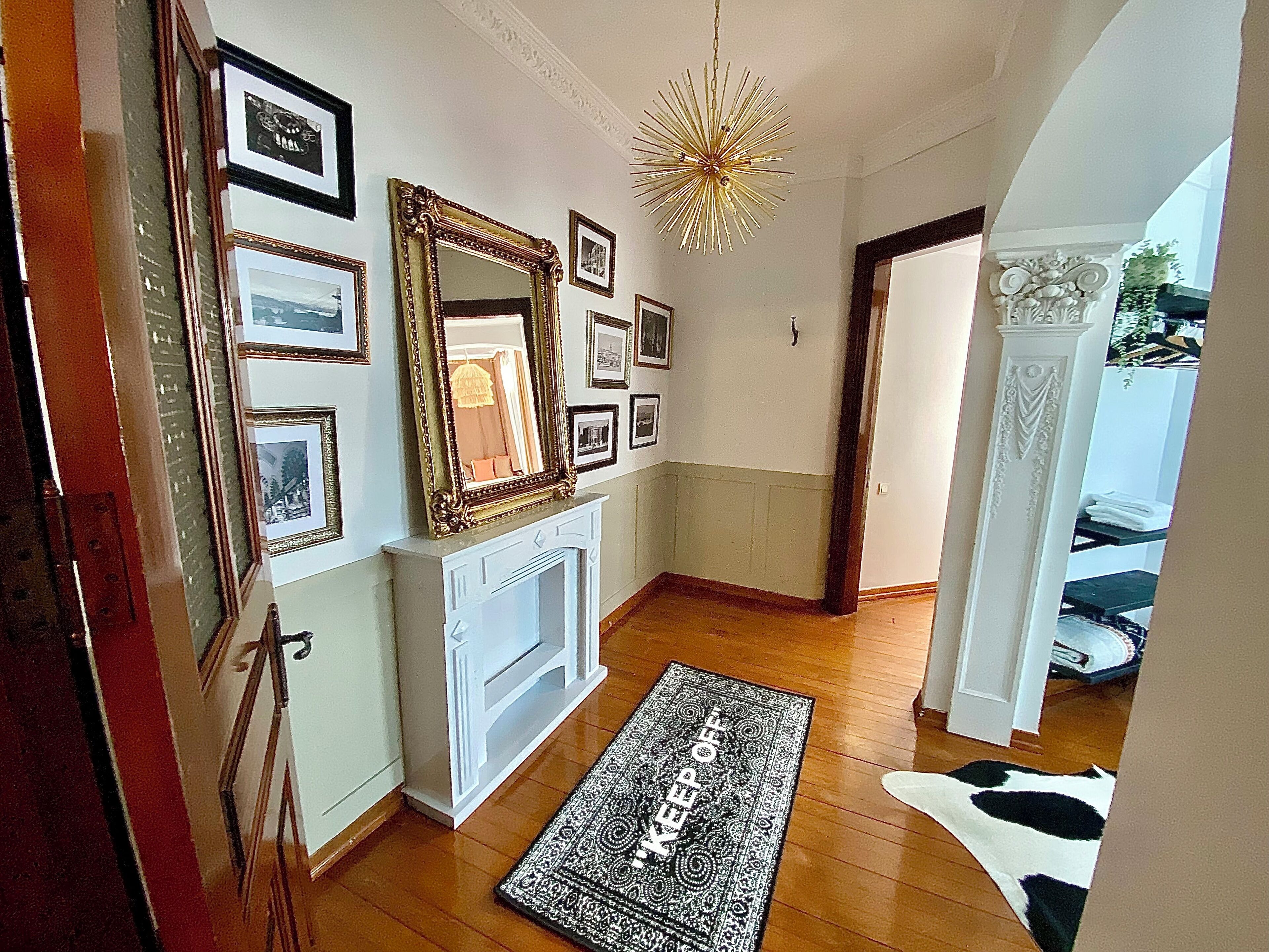A hallway with a fireplace, framed pictures on the wall, a patterned rug, and a cowhide rug on the floor.