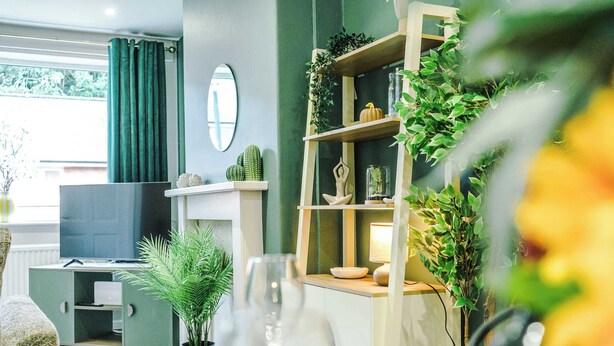 A living room with a TV, green curtains, a bookshelf with plants, and a dining area with a table and chairs. - Stunning Riverside Home in Chester with Parking! (Chester)