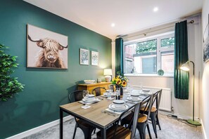 Een eetgedeelte met een tafel voor vier personen, een raam met gordijnen, en een schilderij van een jak op de muur.