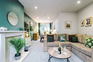 Una sala de estar moderna con un sofá modular, una mesa de centro redonda, una chimenea y un comedor al fondo.