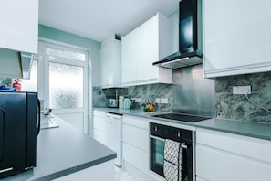 Una cocina moderna con armarios blancos, estufa negra y salpicadero de mármol.