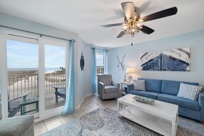 A room with a balcony, a ceiling fan, a sofa, a coffee table, and a painting.
