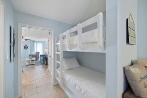 Ein Zimmer mit Etagenbetten, einer Tür zu einem anderen Raum, einem kleinen Tisch und einer Tasche auf einem Nachttisch.