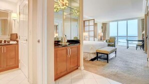 Habitación de hotel con una cama grande, zona de estar, vistas al océano y baño con espejo y armarios.