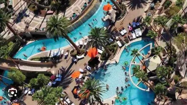 Vista aérea de un resort con varias piscinas rodeadas de palmeras y sillones de descanso.