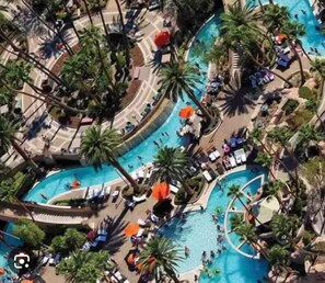 An aerial view of a resort with multiple swimming pools surrounded by palm trees and lounge chairs. - MGM Signature 1BR Condo  Enjoy Pool & Vegas Skyline (Las Vegas)