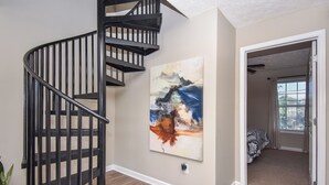 A spiral staircase with a modern design, a large abstract painting on the wall, and a doorway leading to a bedroom with a window.