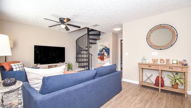 A living room with a blue sofa, a TV, a wooden console table, and a spiral staircase.