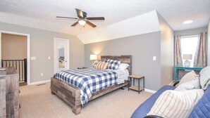 A bedroom with a bed, a ceiling fan, a nightstand, a window with curtains, and a view of the outside.