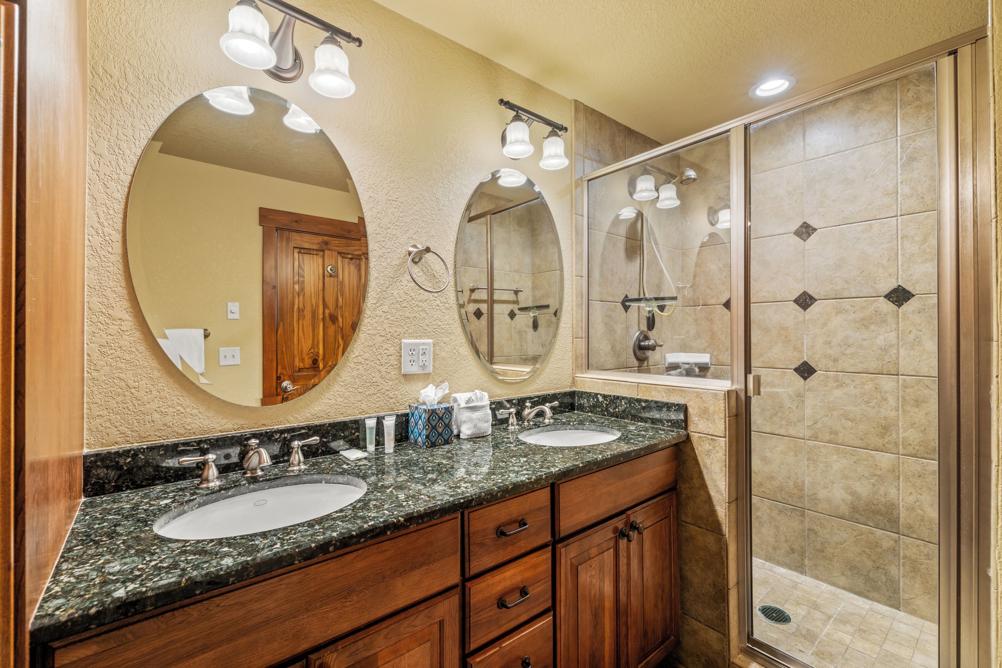 A bathroom with two sinks, wooden cabinets, and a glass-enclosed shower.