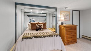A bedroom with a bed, a dresser, a mirror, and a wall-mounted lamp.