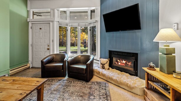 A living room with a fireplace, leather chairs, a TV mounted on the wall, and a view of the outdoors.