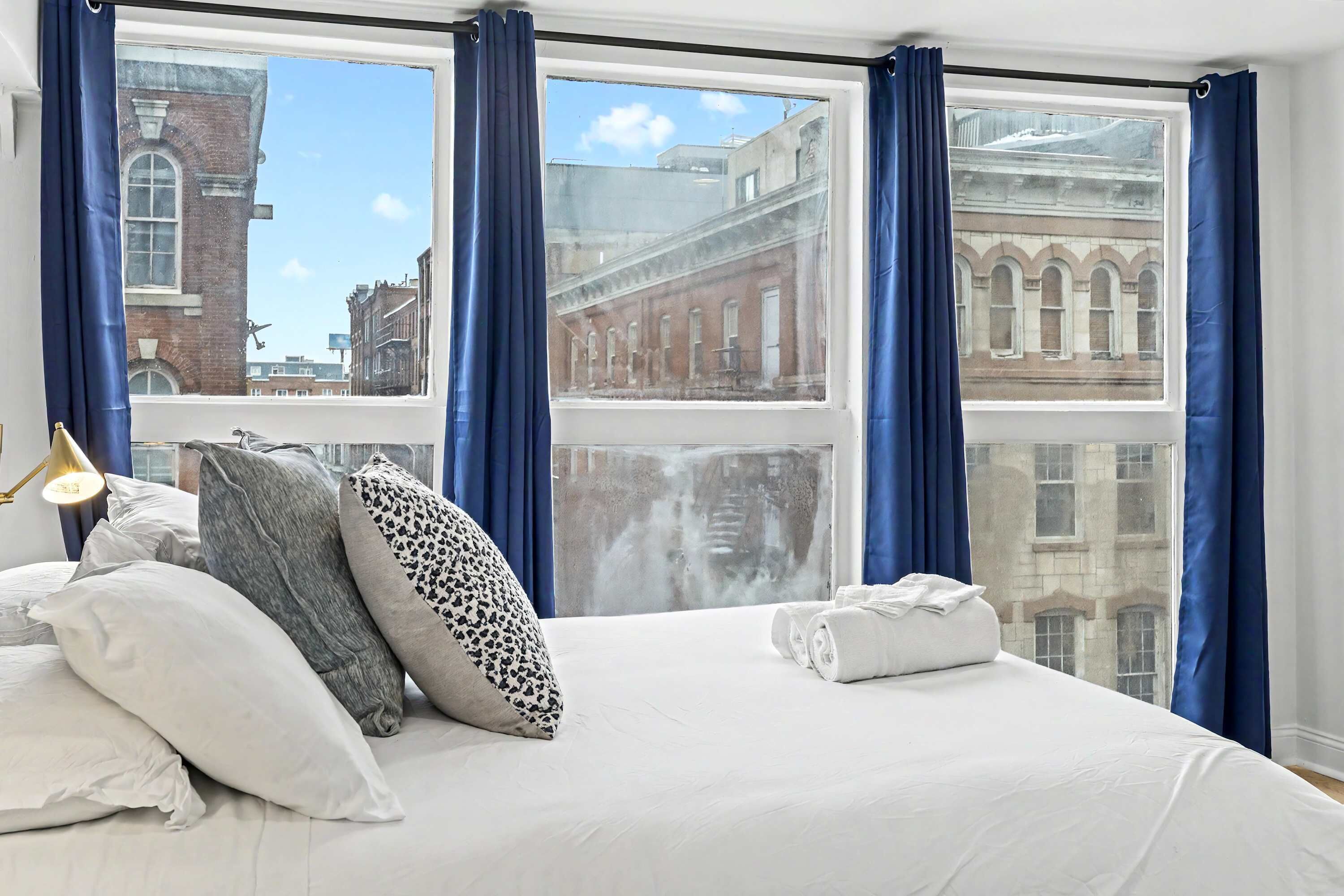 A hotel room with a large bed, blue curtains, and a view of historic buildings.