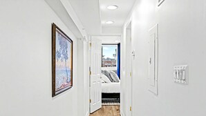 A narrow hallway with white walls, a wooden floor, and a bed with pillows in the background. - Posh Center Spot: 2BR Fits 6 Guests Near Sights (Philadelphia)