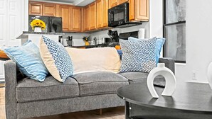 A modern living room with a grey sofa, patterned throw pillows, and a small round table with a white decorative piece. - Posh Center Spot: 2BR Fits 6 Guests Near Sights (Philadelphia)