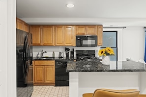 A modern kitchen with wooden cabinets, a black refrigerator, a microwave, a dishwasher, and a granite countertop. - Prime 2BR Sleeps 6 Oasis | Near The Liberty Bell (Philadelphia)