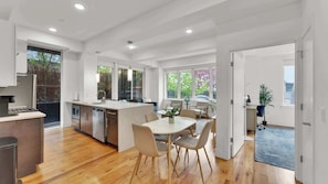 Una cocina moderna con comedor, piso de madera y ventanas amplias.