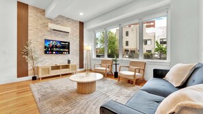 Un salon moderne doté d’un téléviseur à écran plat, de meubles en bois, d’une table basse ronde et de grandes fenêtres offrant une vue sur la ville.