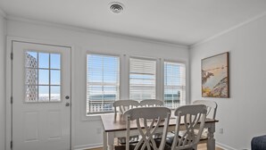 A dining area with a wooden table and chairs, a white door, and windows with blinds. - Classic Oceanfront Beach Cottage! (Emerald Isle)