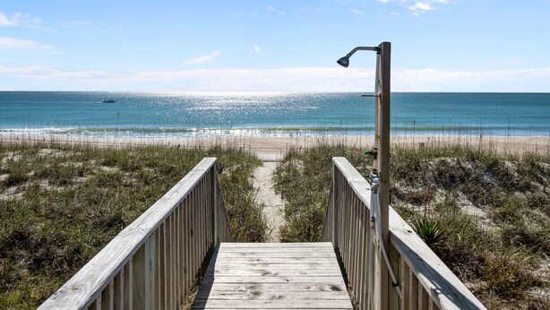 A wooden boardwalk leading to a beach with a clear view of the ocean and a boat in the distance. - Classic Oceanfront Beach Cottage! (Emerald Isle)